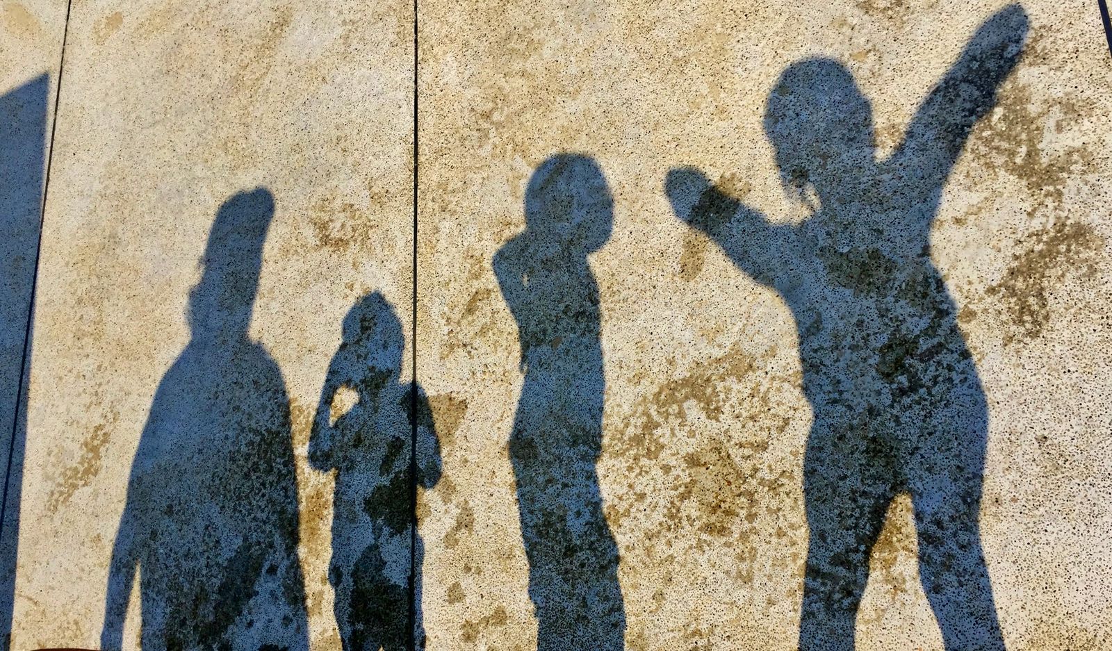 Four shadows thrown across a concrete wall, one arm raised