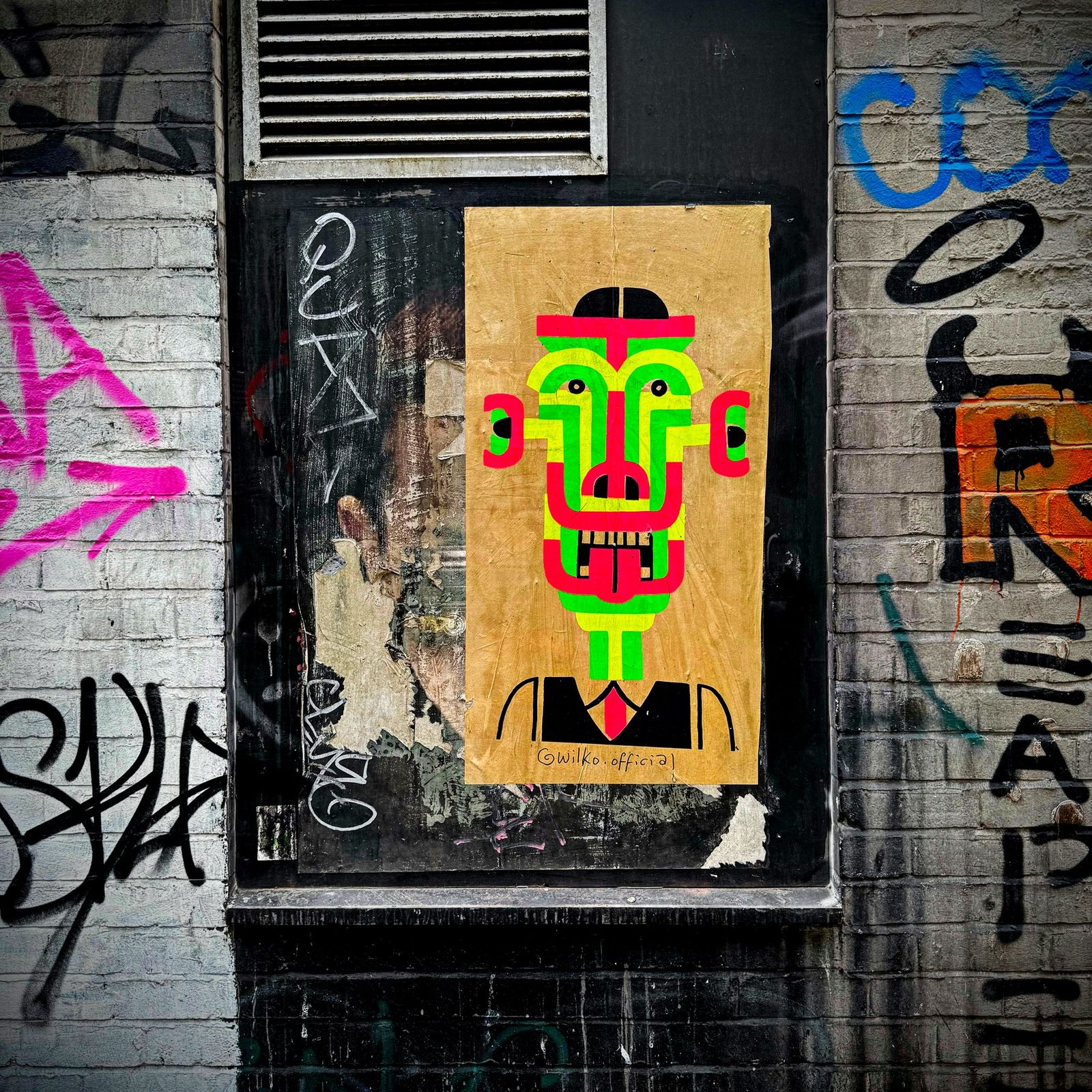 A pasted paper face among the tags on a city wall