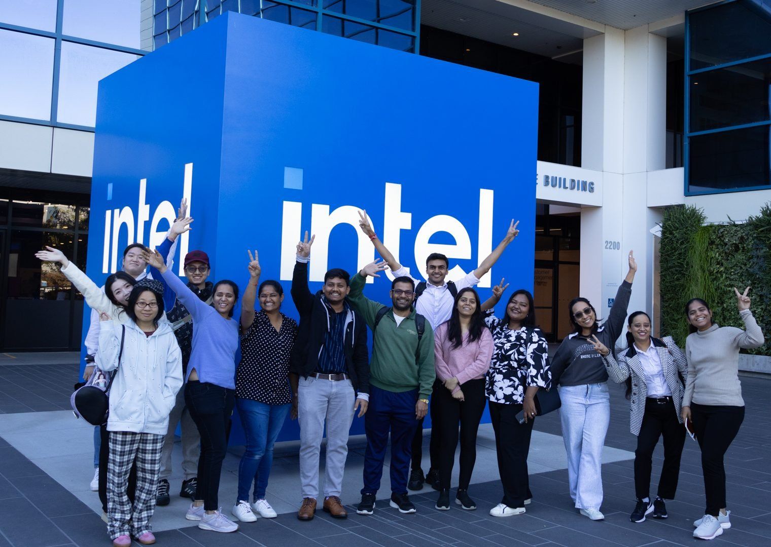 A group of SFBU students posing with arms raised in front of the large blue Intel logo cube outside Intel headquarters