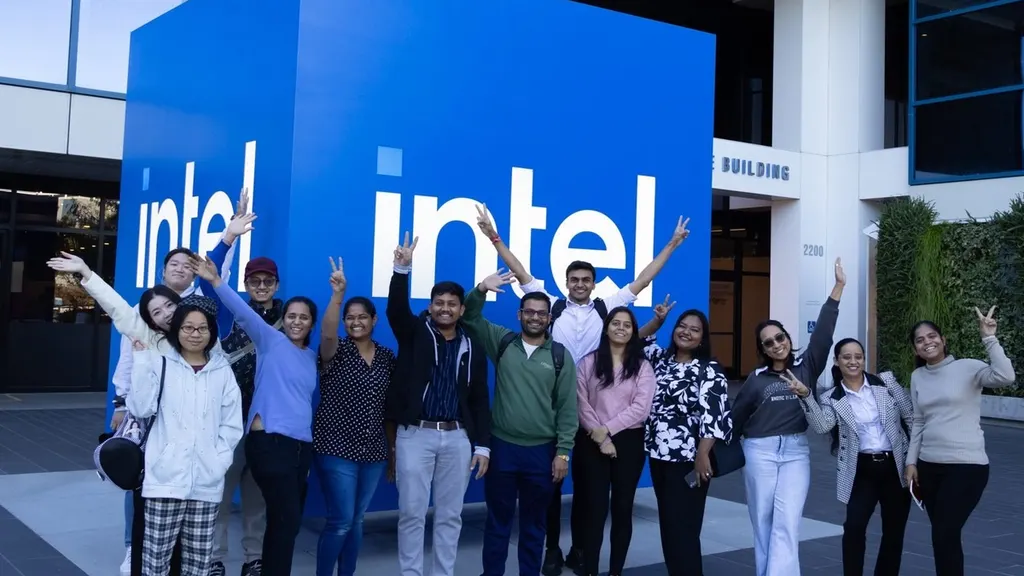 A group of SFBU students posing with arms raised in front of the large blue Intel logo cube outside Intel headquarters