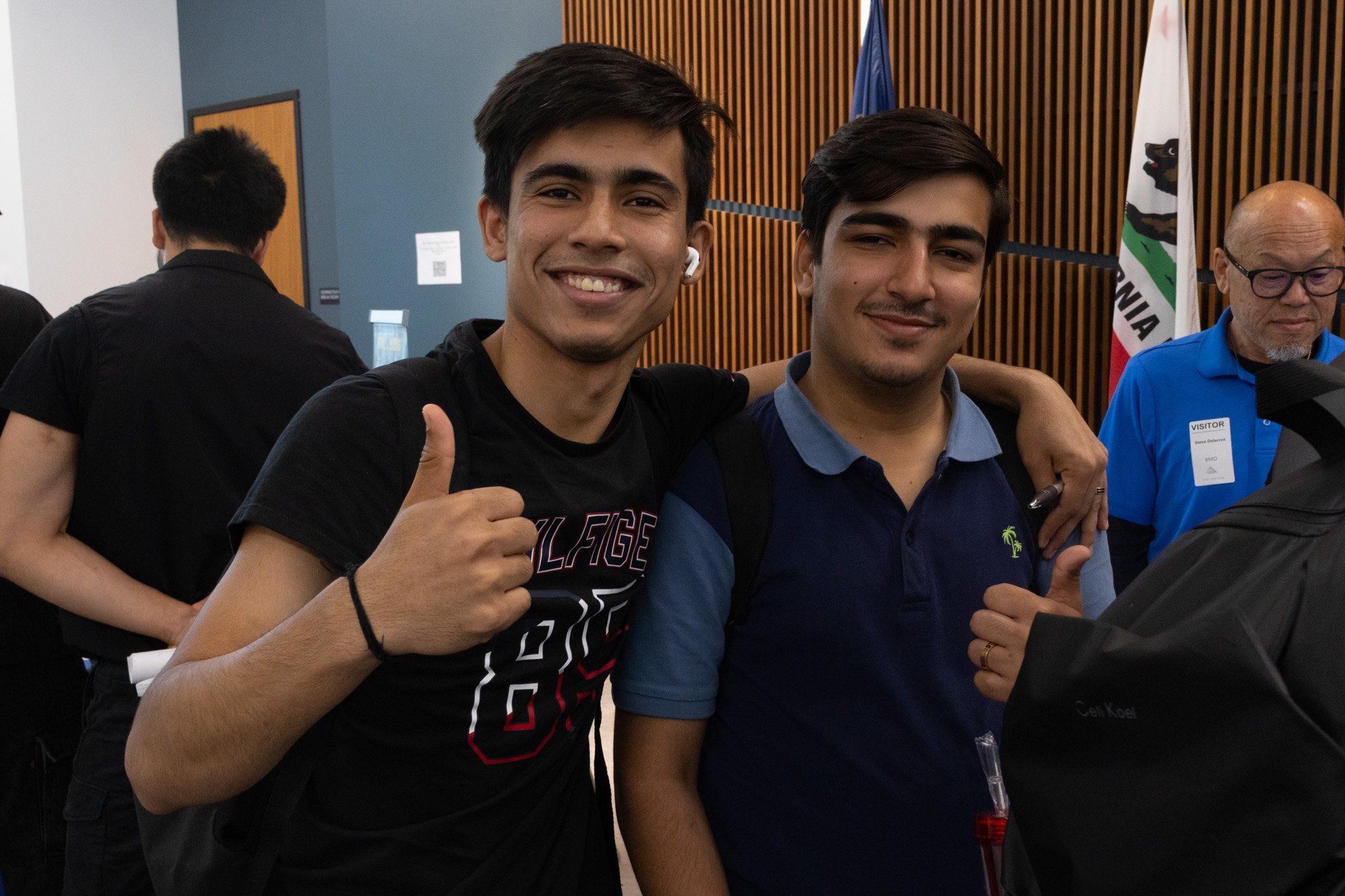 Two SFBU students standing together at an indoor campus career fair, one giving a thumbs up to the camera