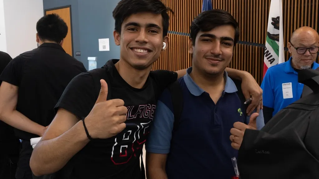 Two SFBU students standing together at an indoor campus career fair, one giving a thumbs up to the camera