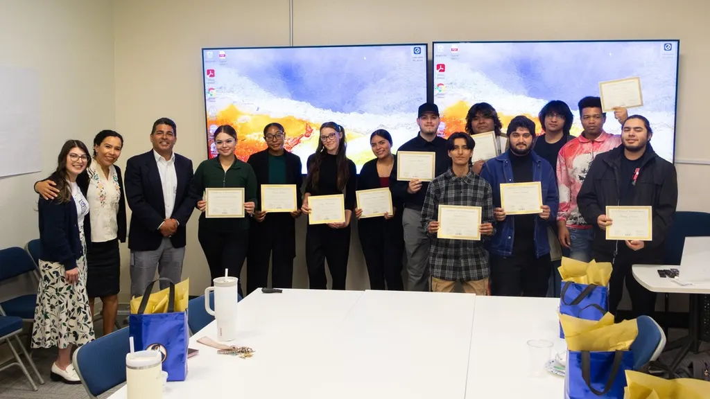 A group of SFBU students standing with framed certificates alongside faculty in a classroom, with presentation screens behind them