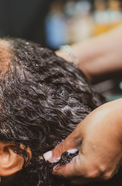 A curly-haired client getting her hair shampooed in a professional salon setting.