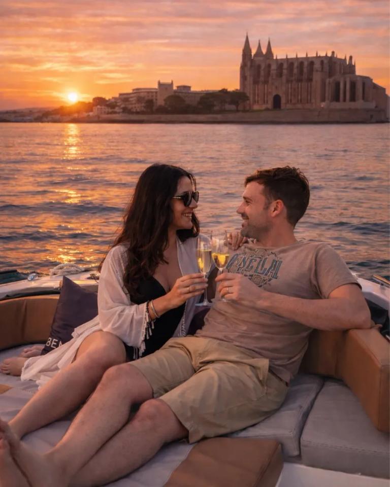 Pareja brindando con cava a bordo frente a la catedral de Palma al atardecer.