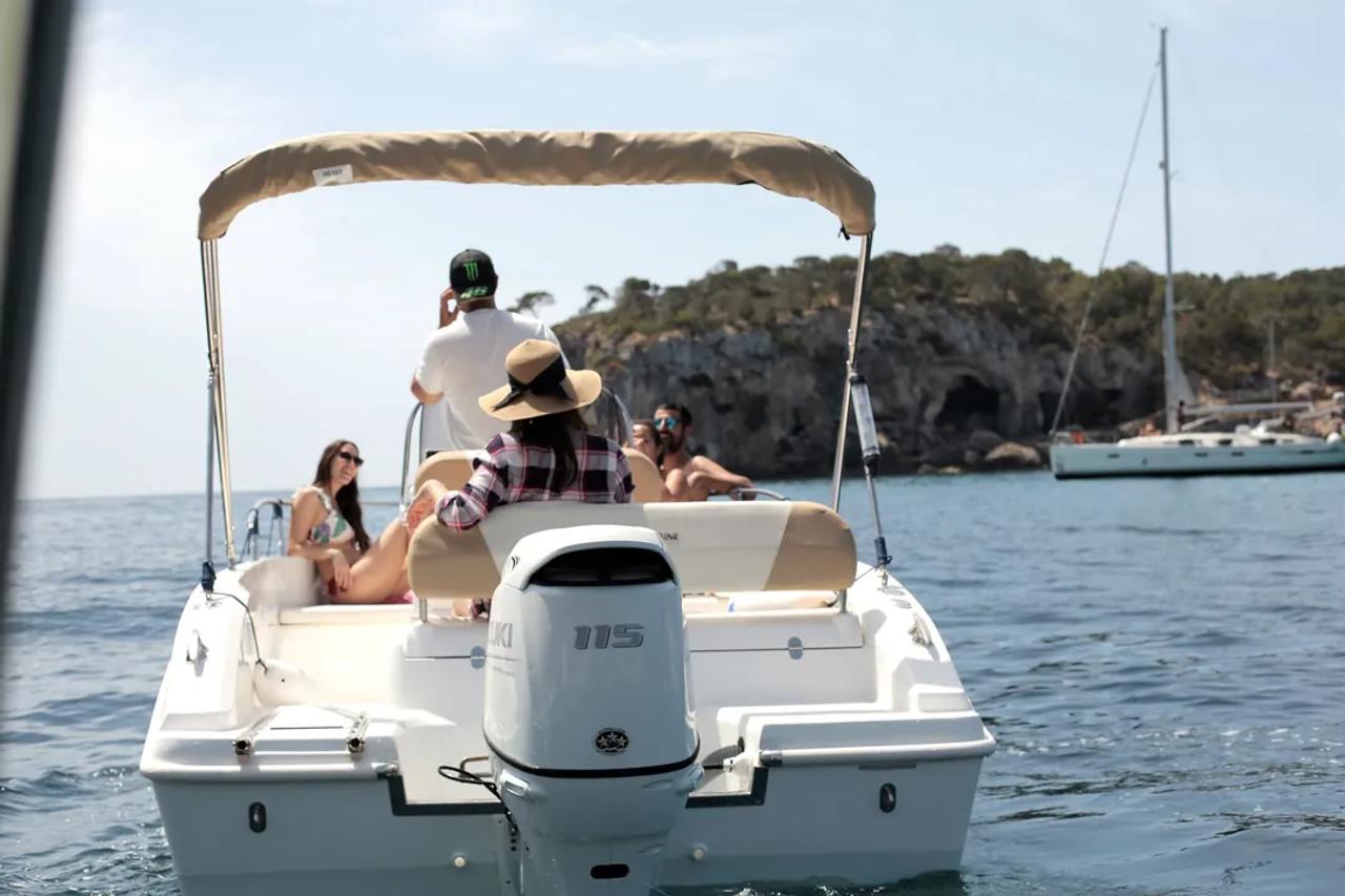 La barca fondeada en una cala recogida, con un velero al fondo.