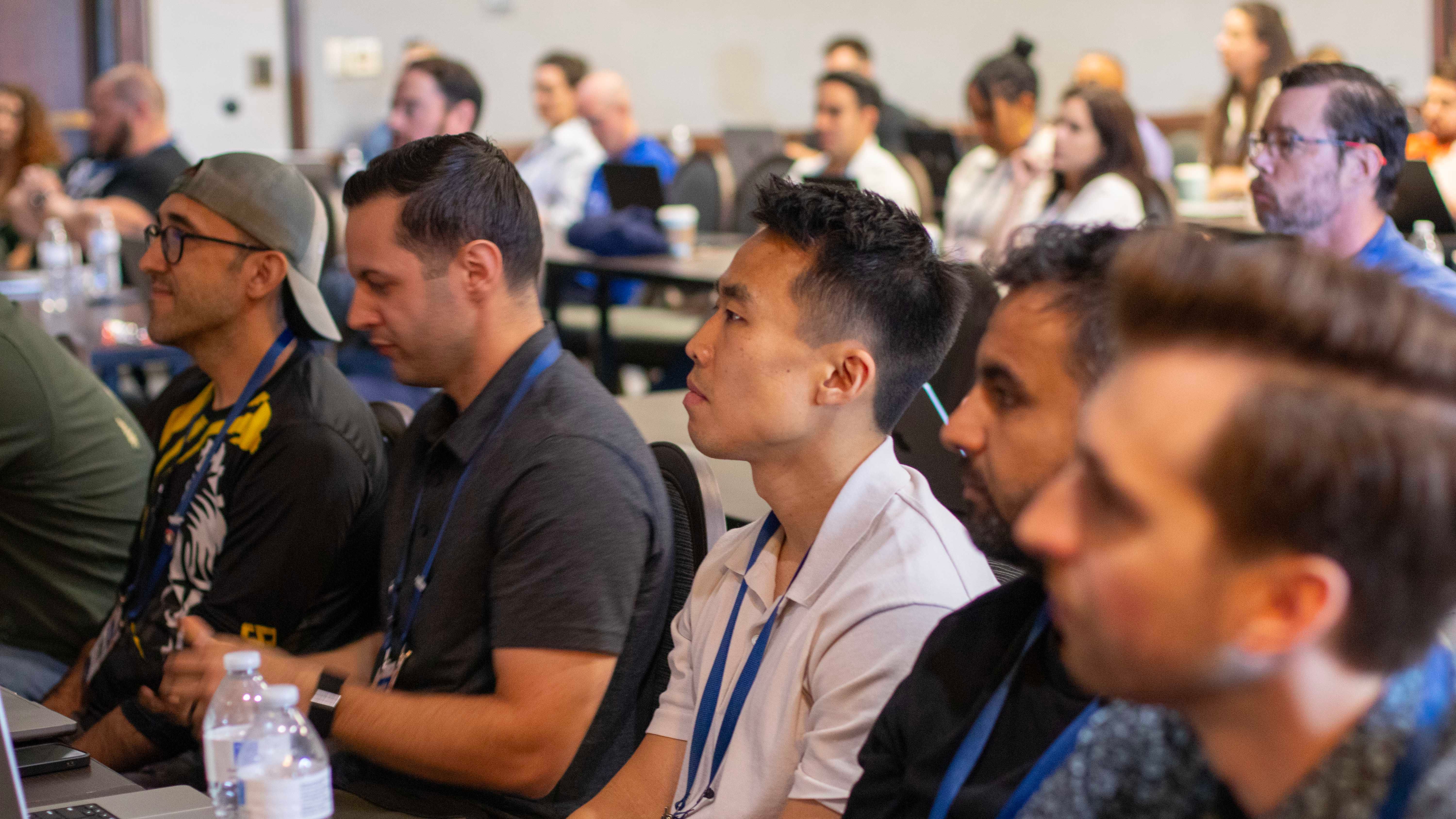 Attendees seated at a training session, watching a speaker, lanyards around their necks.
