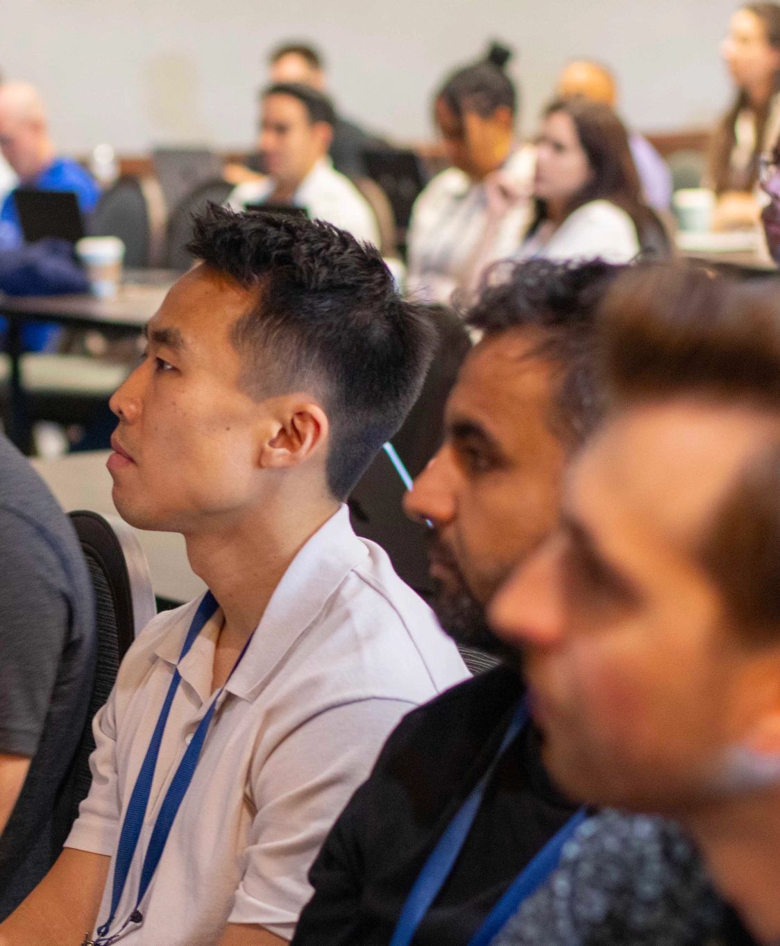 Attendees seated at a training session, watching a speaker, lanyards around their necks.
