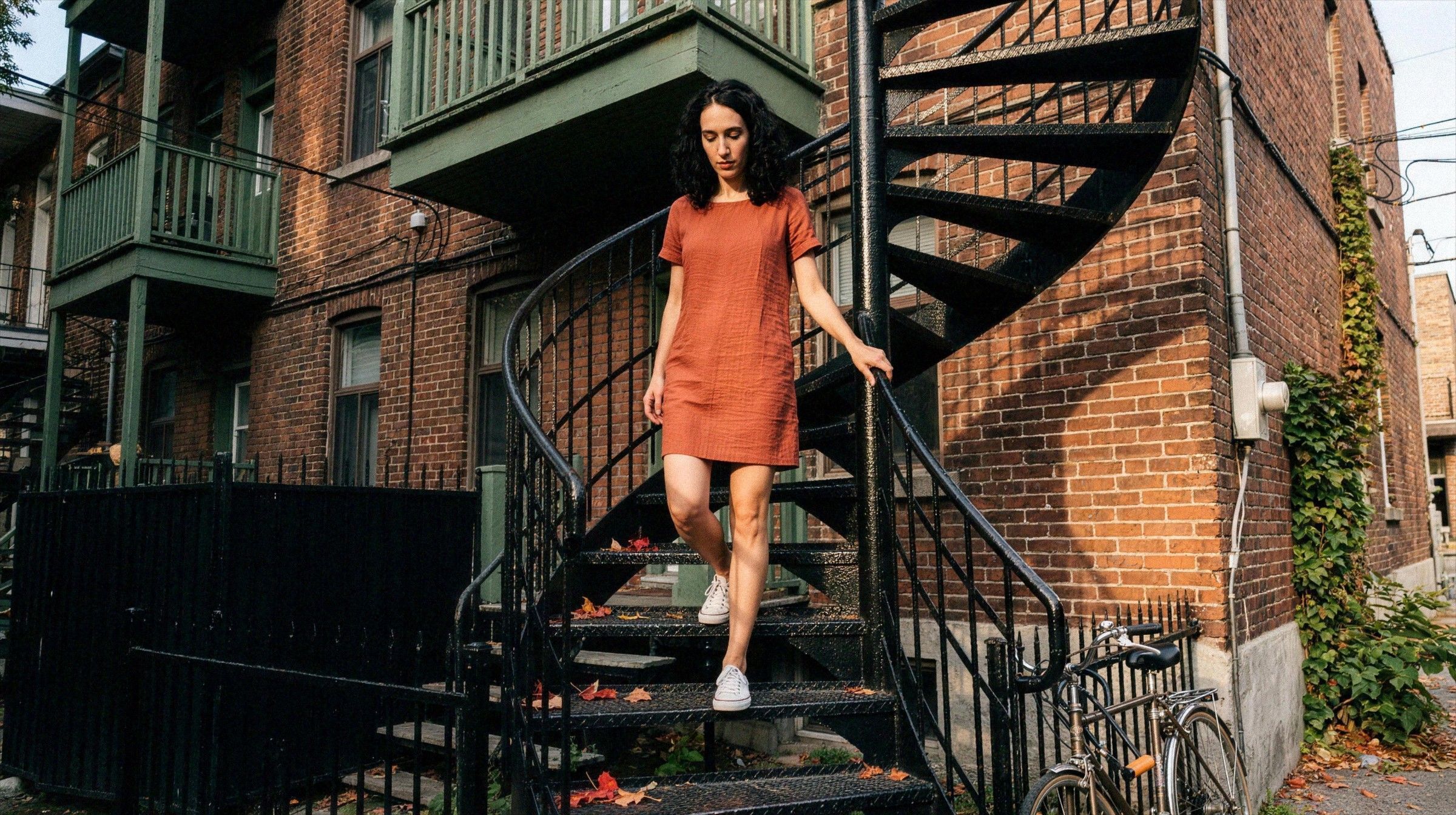 A woman in a sleeveless dress walks down an outdoor spiral staircase on a Plateau street in Montreal.