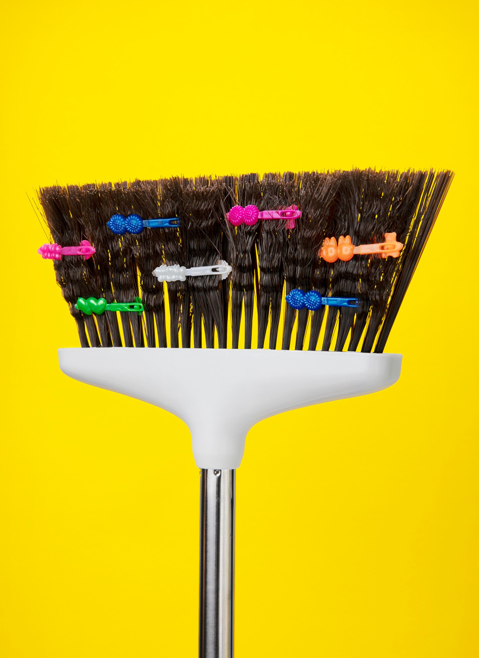 A broom with crimped bristles and colorful butterfly hair clips.