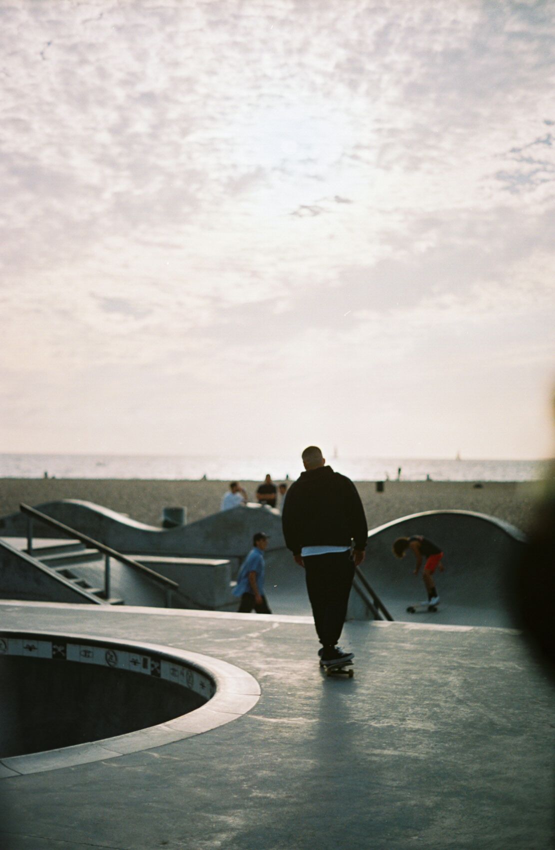 A skateboarder at the skate park at Venice Beach. A sunny sky and sandy beach are in the background.