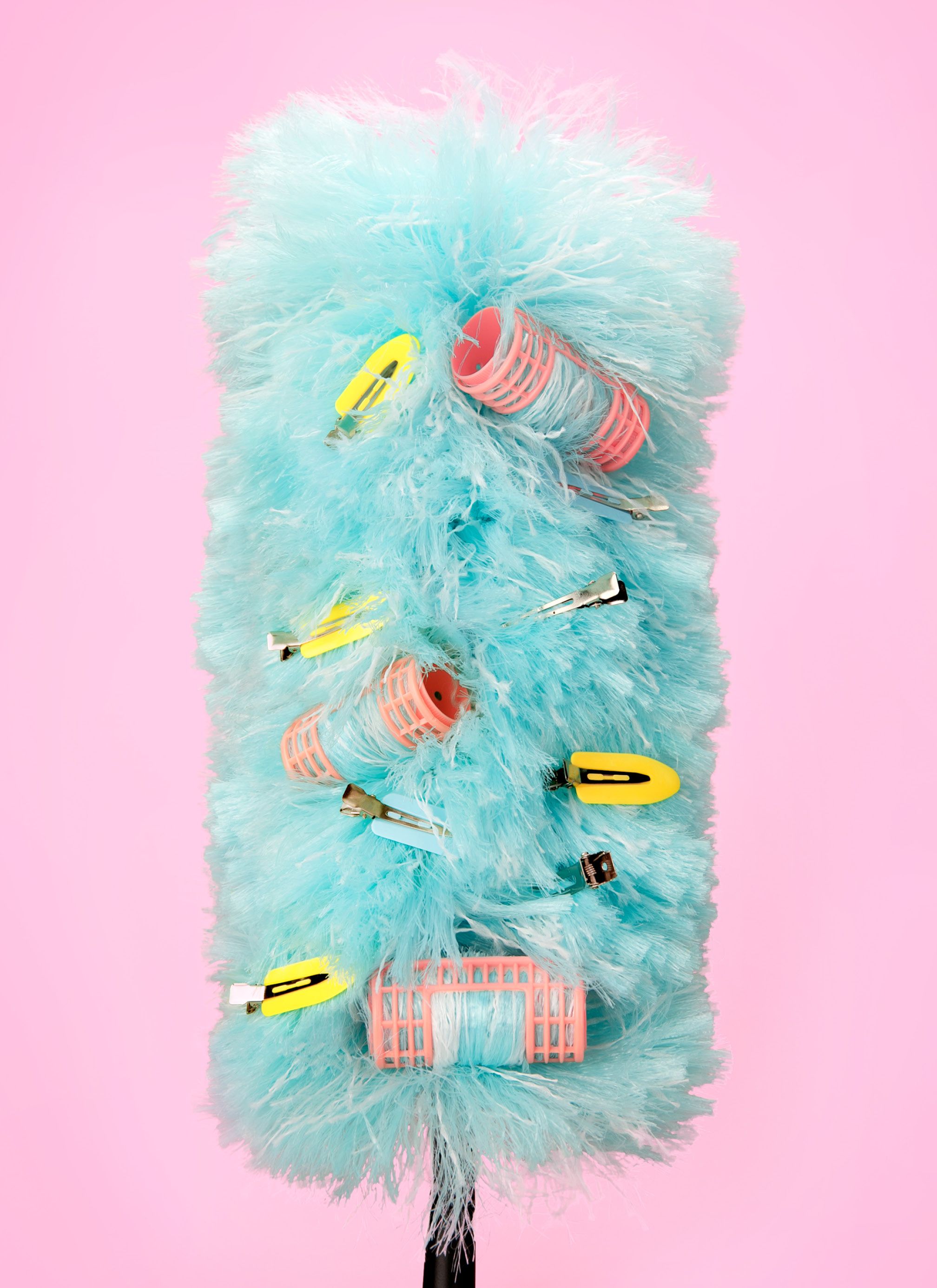 A fluffy blue feather duster with pink and yellow hair curlers and clips in its feathers.