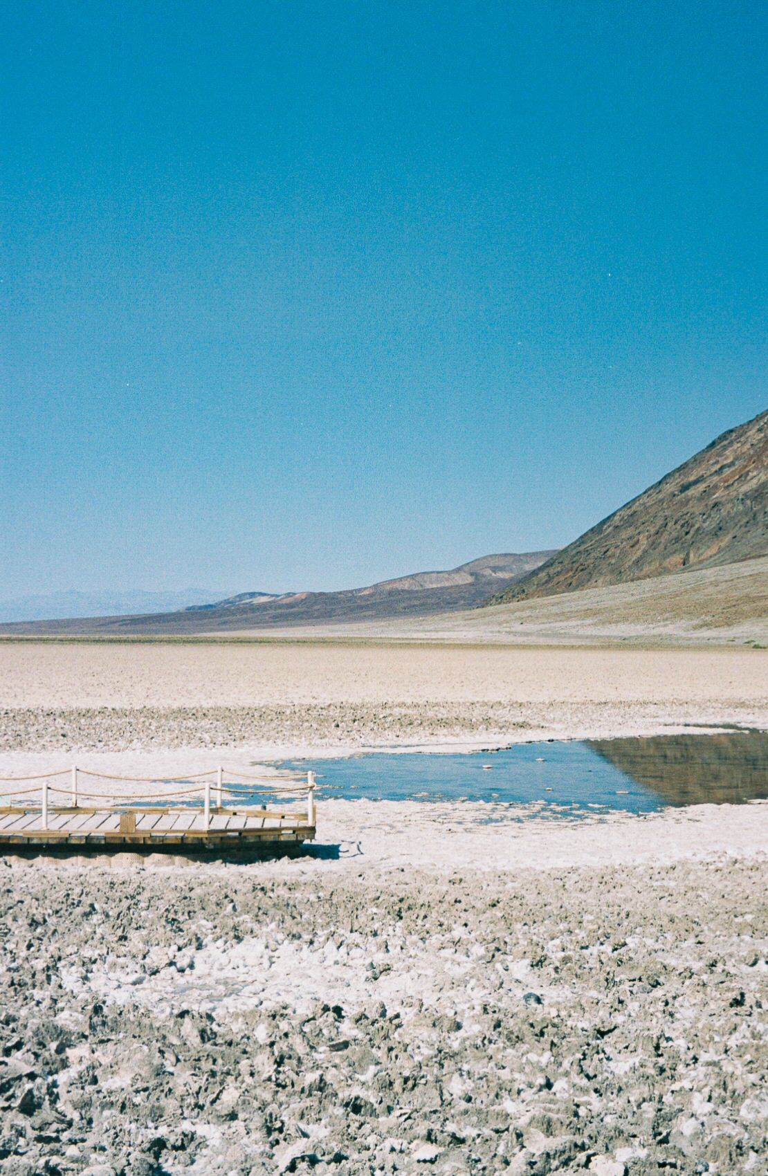 A wooden walkway next to a small pool of standing water at the salt plain floor of Death Valley