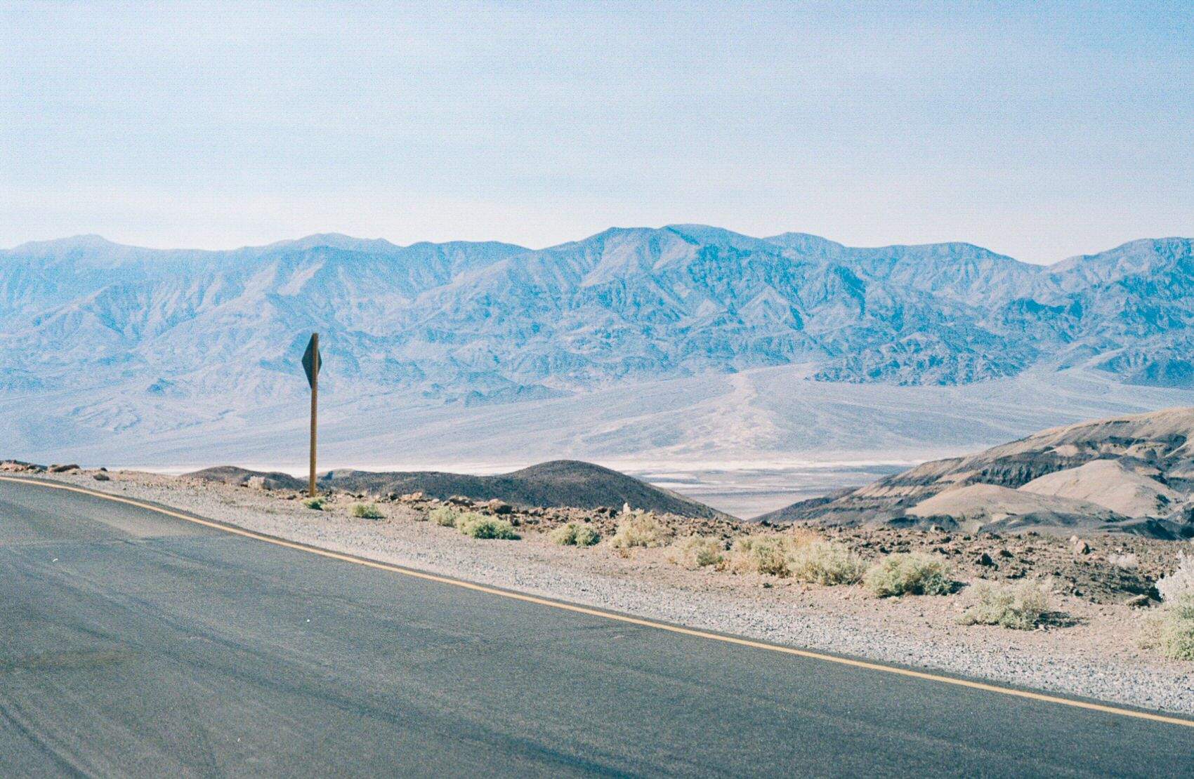 A road and street sign. In the background is Death Valley and its surrounding mountains.