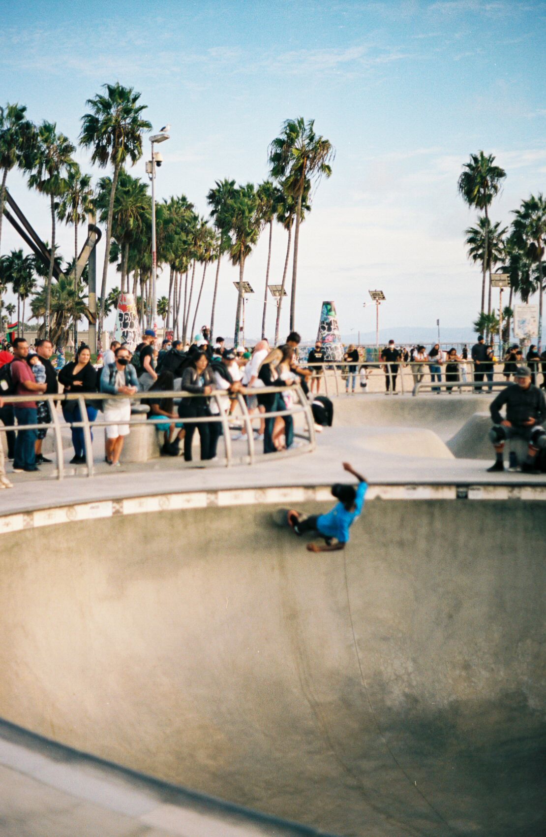 A skateboarder skates a pool at the skate park in Venice Beach as a crowd of people watches.