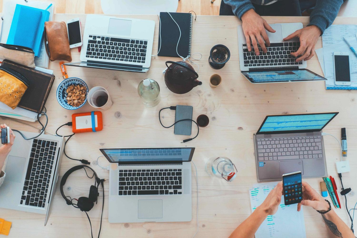 four people working on a table with their laptops open