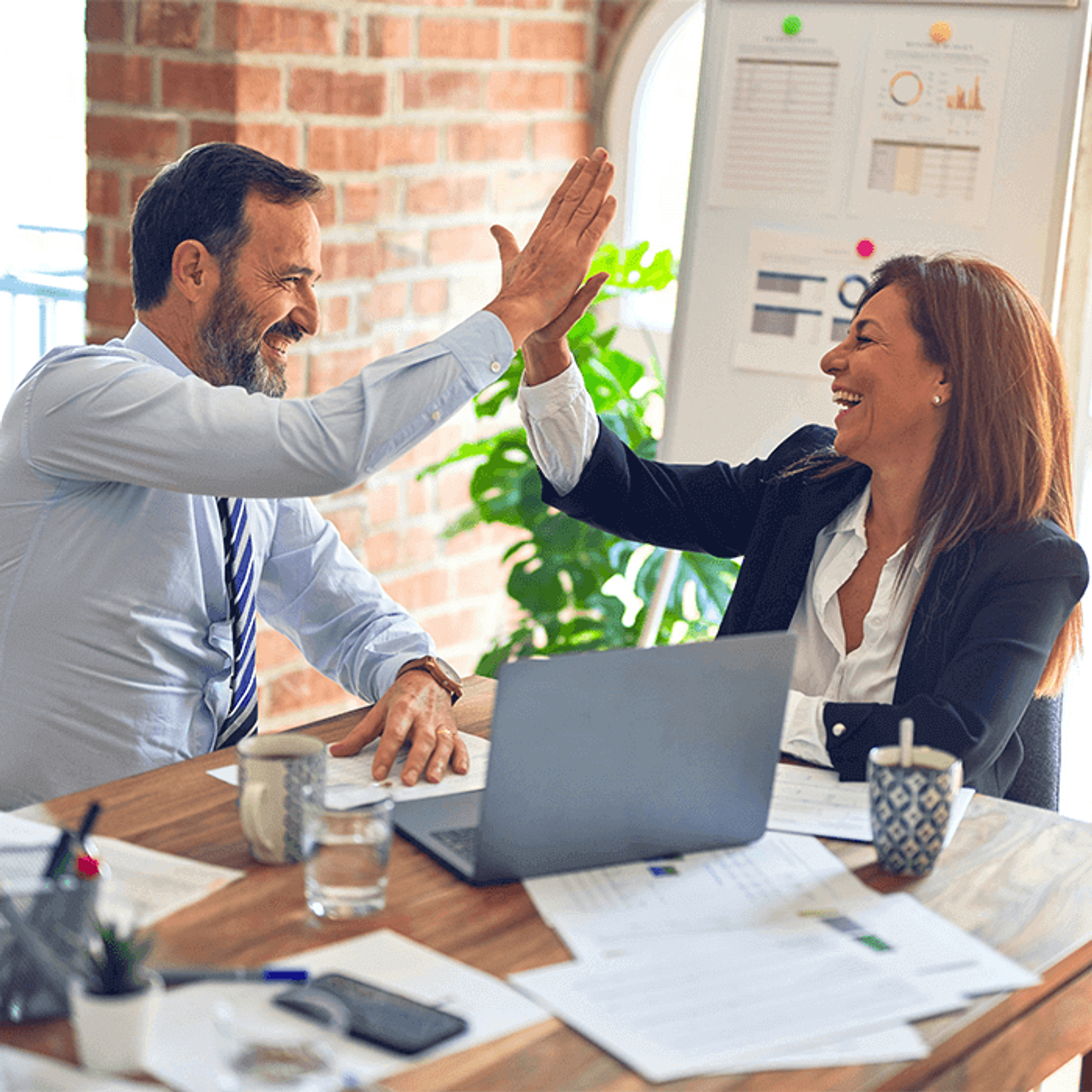 Co-workers celebrate a successful exit negotiation with a high-five, symbolizing teamwork and success
