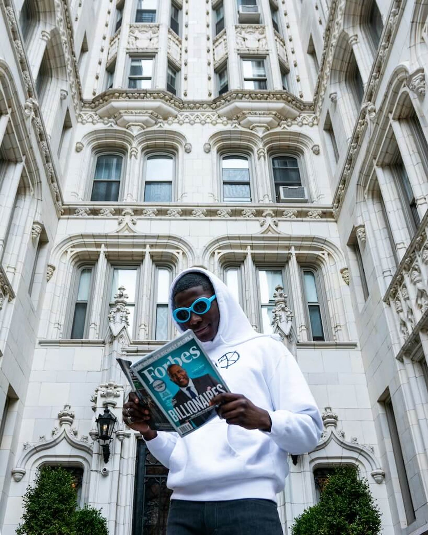 A young entrepreneur holds a Forbes magazine, confidently, symbolizing startup success.