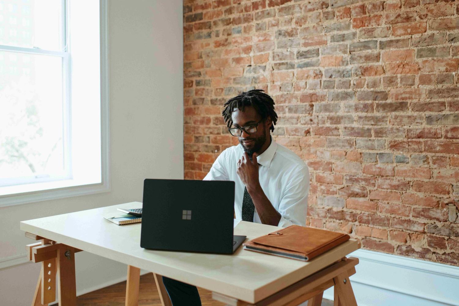 A black male looking at his laptop while working in his office
