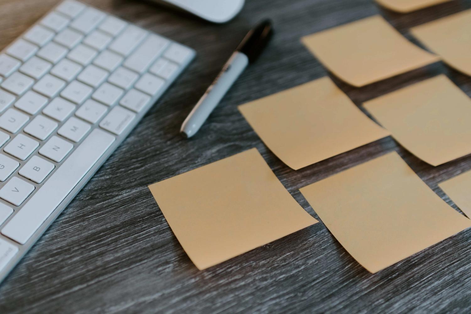 Multiple sticky notes put on a office desk next to a keyboard and a pensil