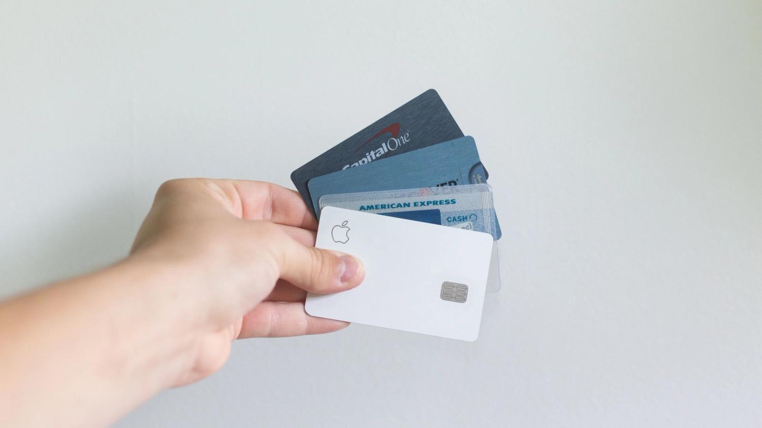 a hand holding four different credit cards on a white wall in the background