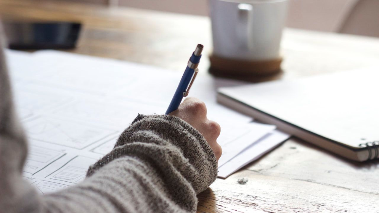 Close-up of a student's hand writing notes at a desk with study papers and a notebook, representing intensive last-minute exam preparation