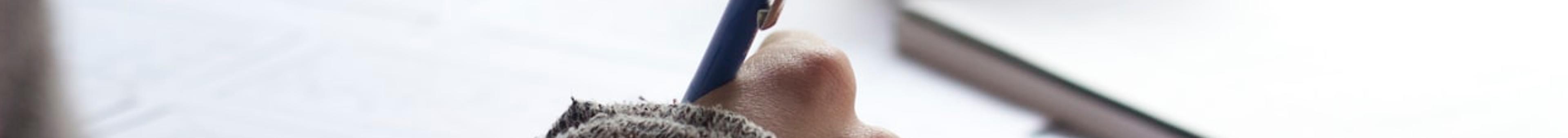Close-up of a student's hand writing notes at a desk with study papers and a notebook, representing intensive last-minute exam preparation