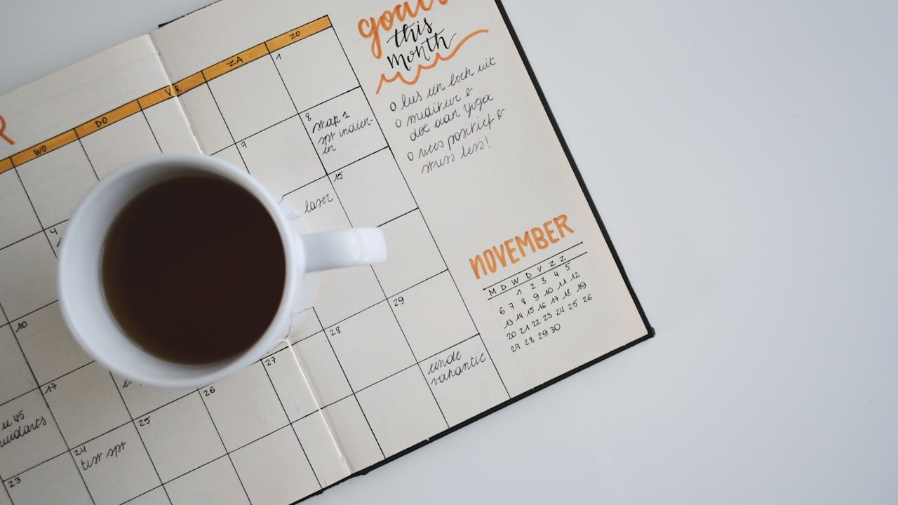 Monthly planner open to a November calendar page with handwritten goals and a white coffee mug, representing exam date planning and scheduling