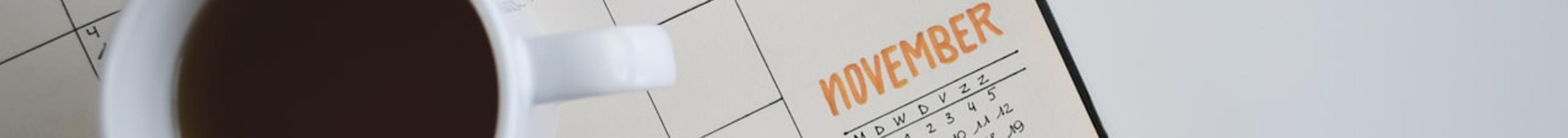 Monthly planner open to a November calendar page with handwritten goals and a white coffee mug, representing exam date planning and scheduling