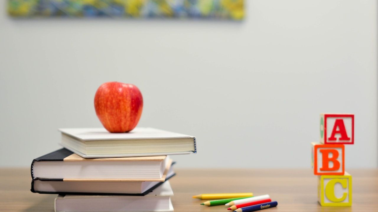 Stack of books with an apple on top, alphabet blocks, and coloured pencils on a desk — a language and learning study scene