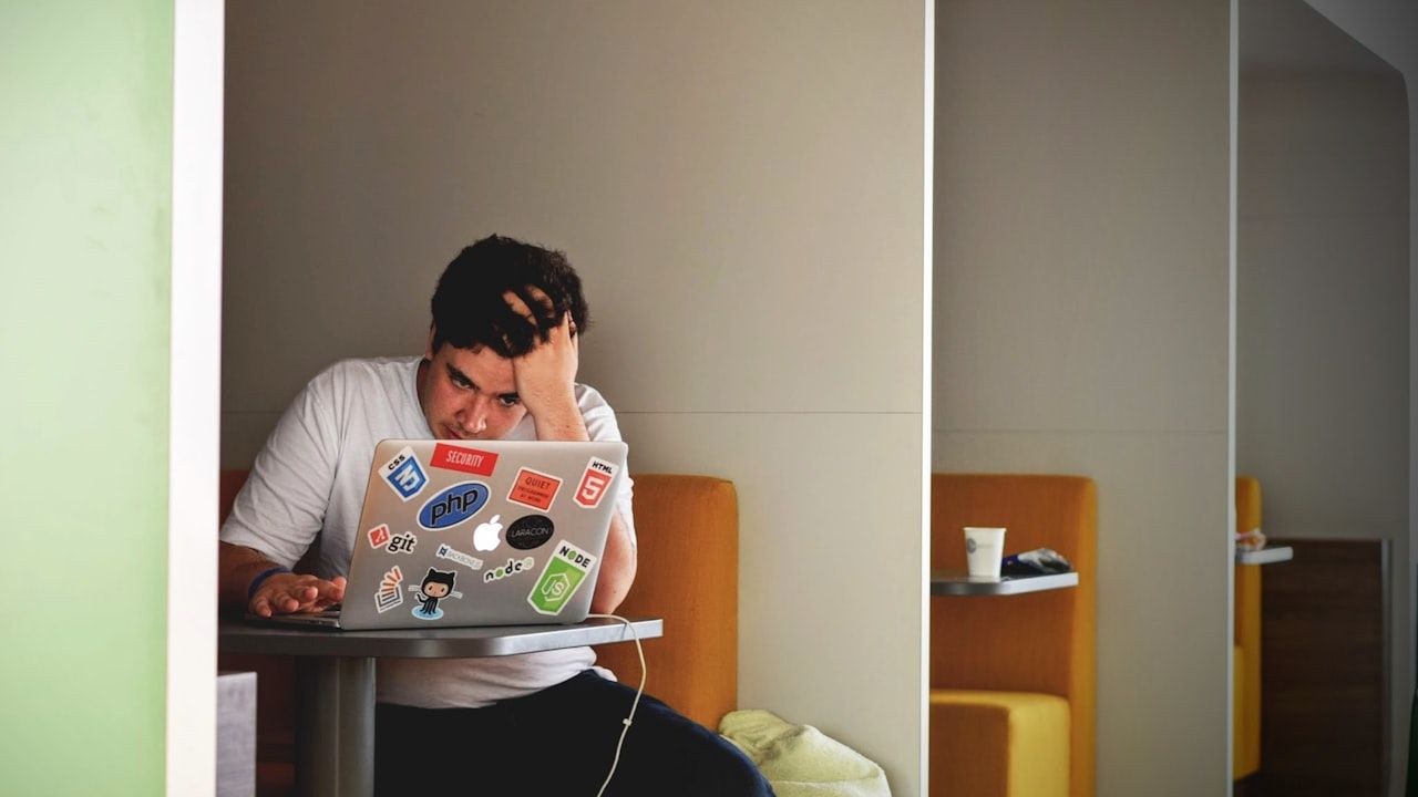 A student leaning over a laptop with head in hand, studying intensely under deadline pressure