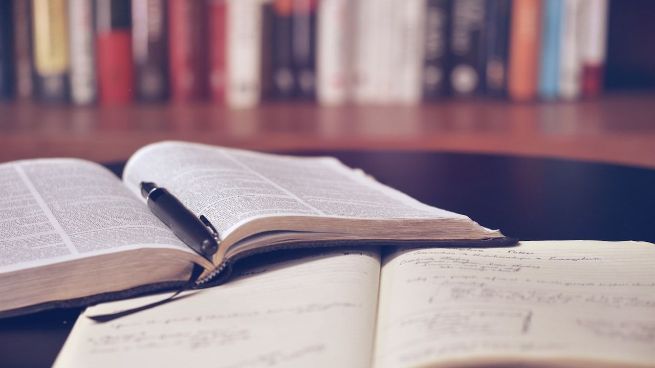Open textbooks and handwritten notes on a desk with a bookshelf in the background, representing MDCAT study preparation