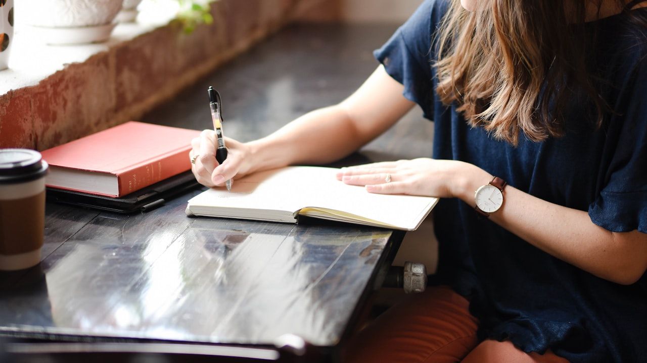 Student writing in a notebook at a desk with books and coffee, representing English grammar practice