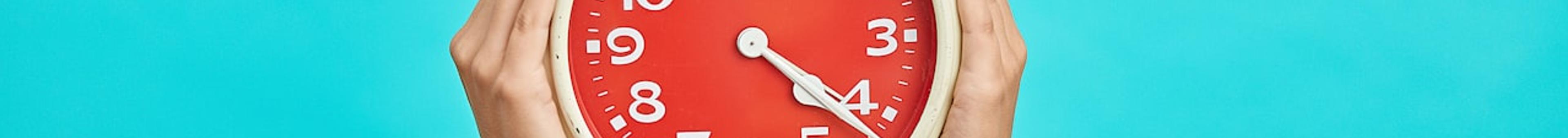 Hands holding a red alarm clock against a teal background, representing time management in the MDCAT exam