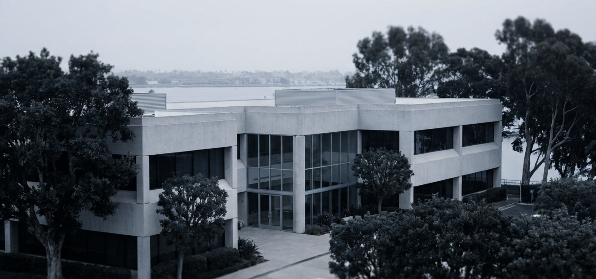 A low-rise Southern California office building on the water, seen through mature trees.