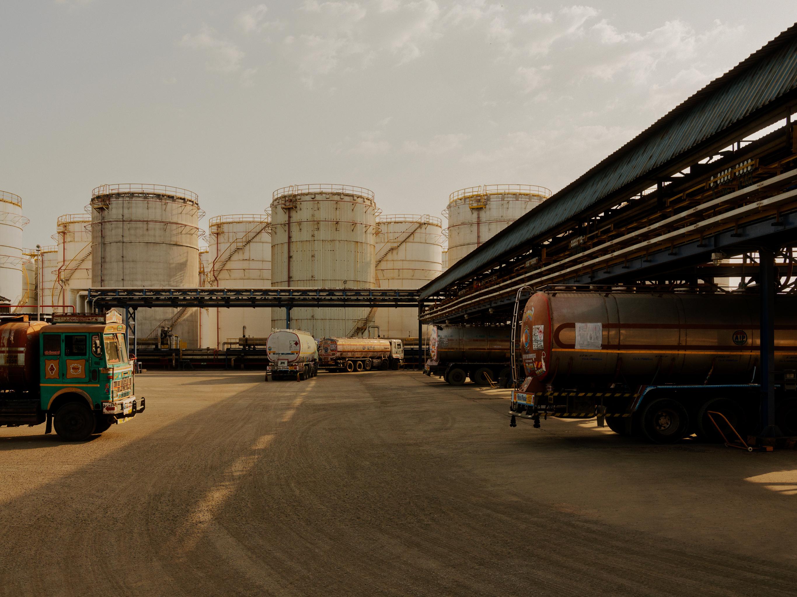 Trucks pulling into gantry with liquid tanks in the background.
