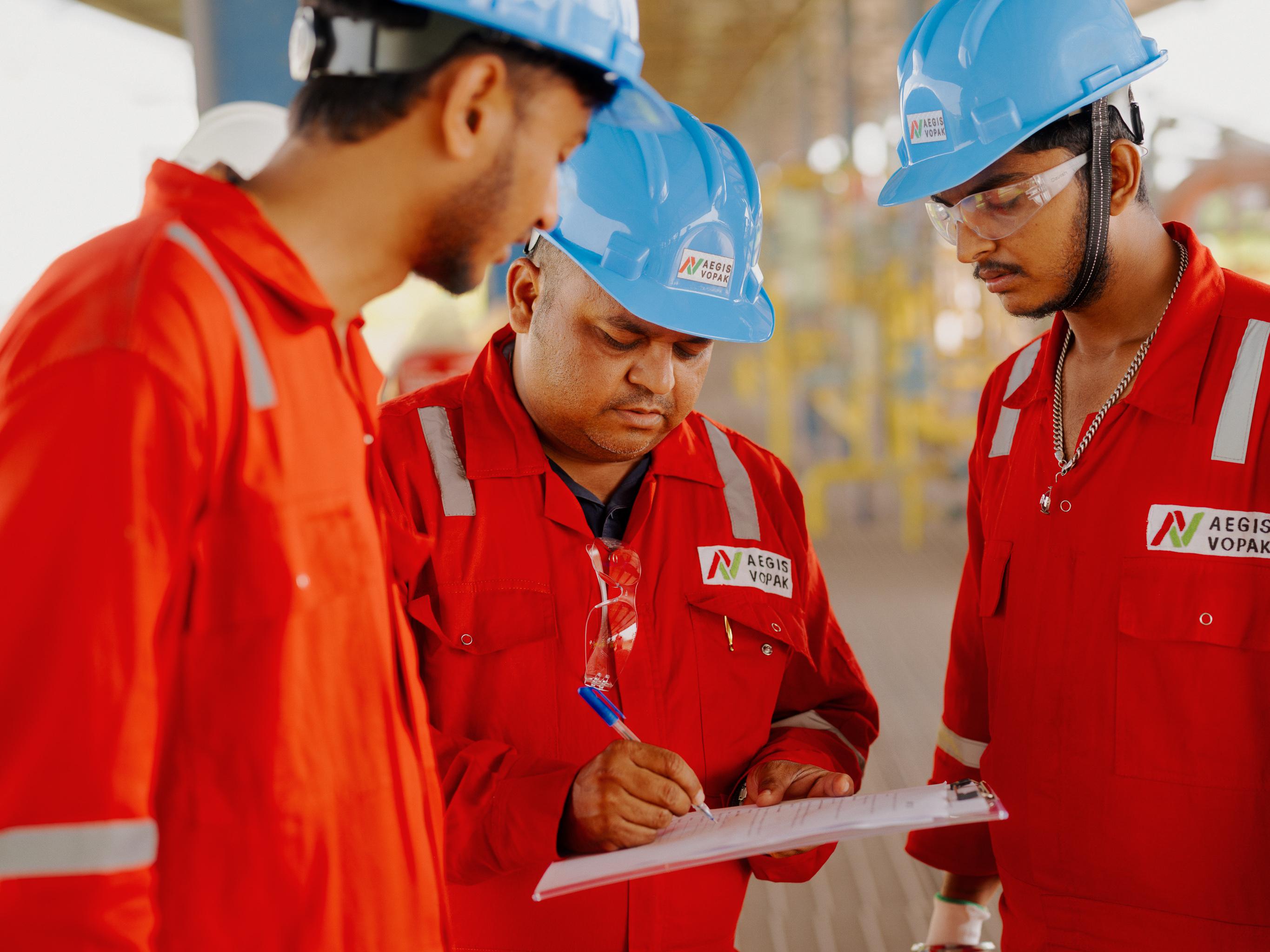 Three AVTL workers look at a clipboard, with one of them writing.