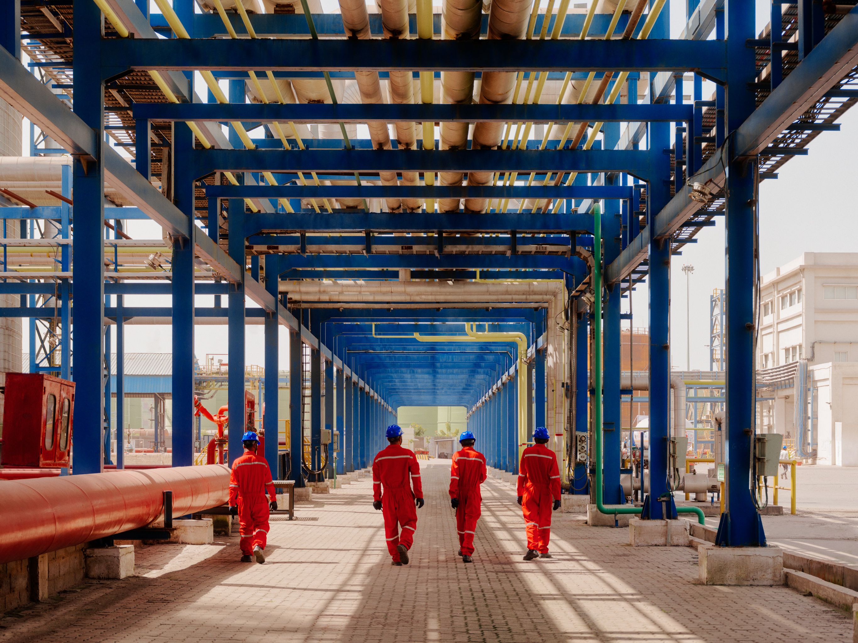 4 AVTL workers walk under a corridor of pipes at the Kandla terminal.