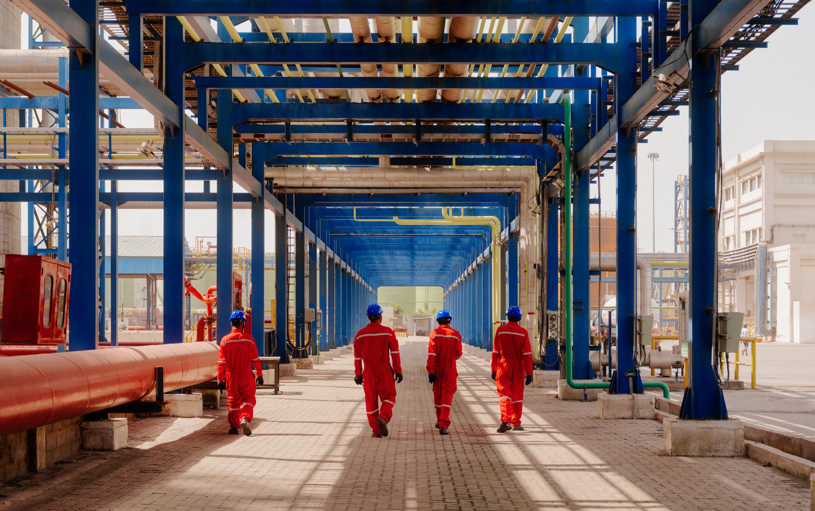 4 AVTL workers walk under a corridor of pipes at the Kandla terminal.
