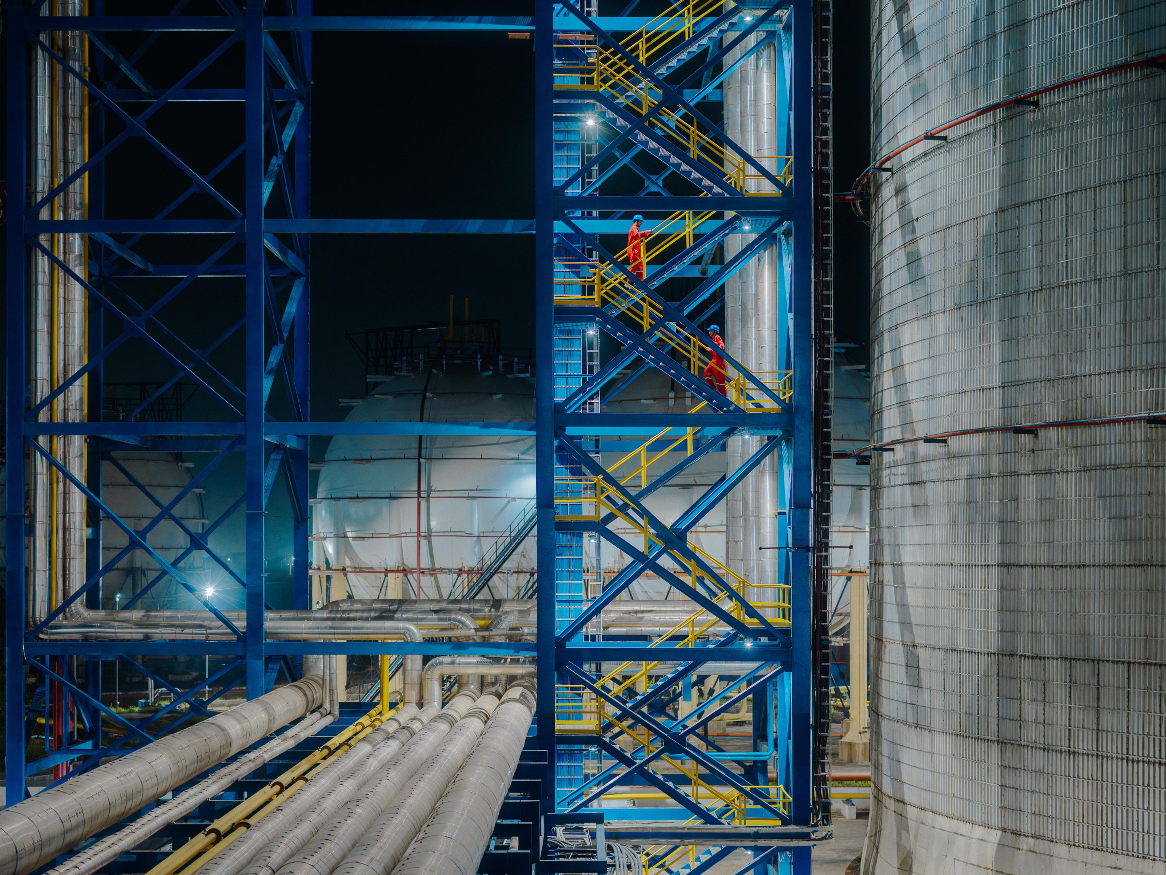 Two AVTL workers descend down a staircase alongside a storage tank, at night.