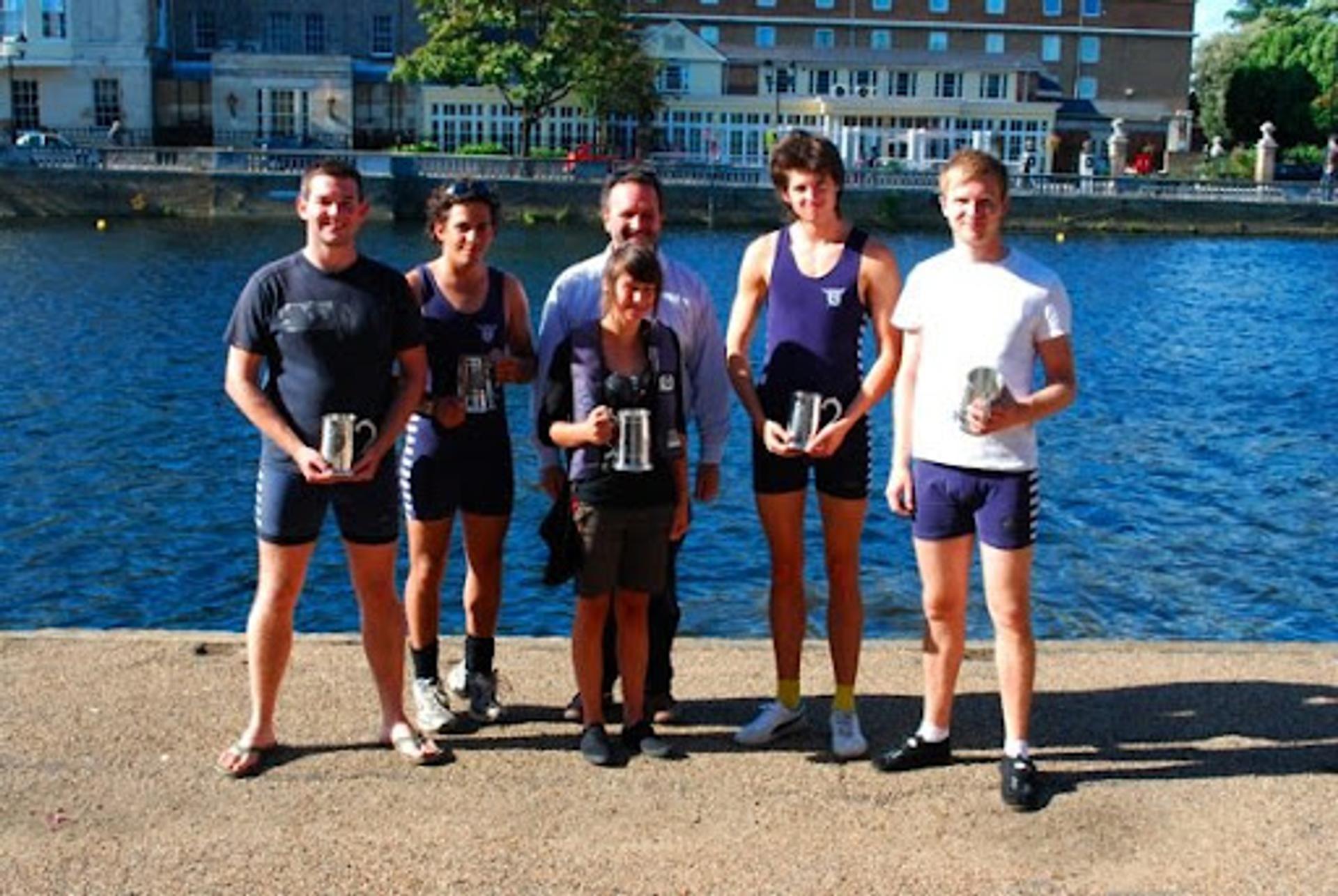 The successful coxed four, holding their pots by the river. 