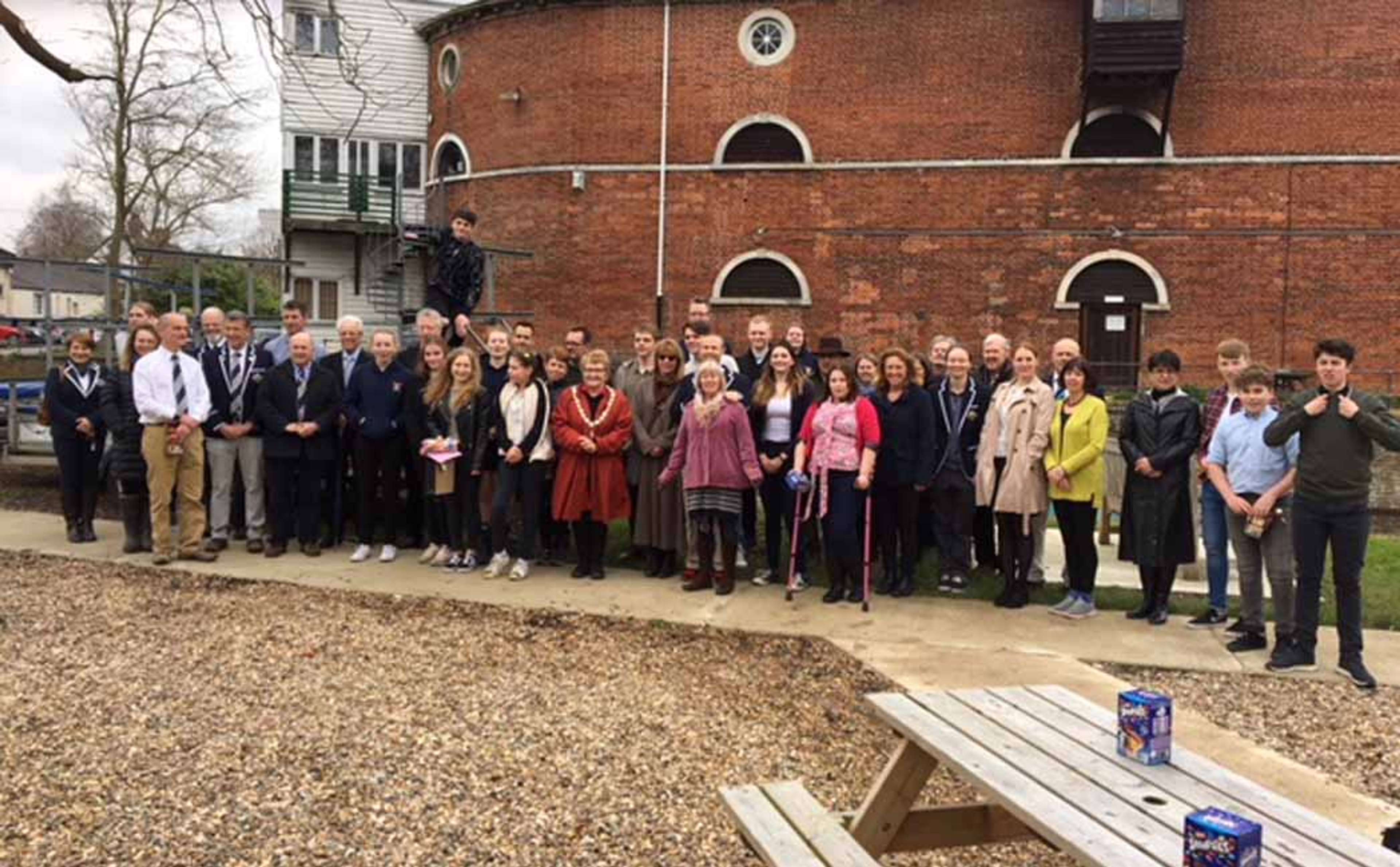 Members assemble for the Good Friday Opening, pictured on the gravel between the boathouse and cut, with the large brick structure of the Quay Theatre in the background.