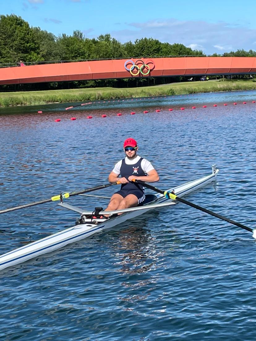 A male single sculler passing the olympic ring motif at the Dorney rowing lake. 