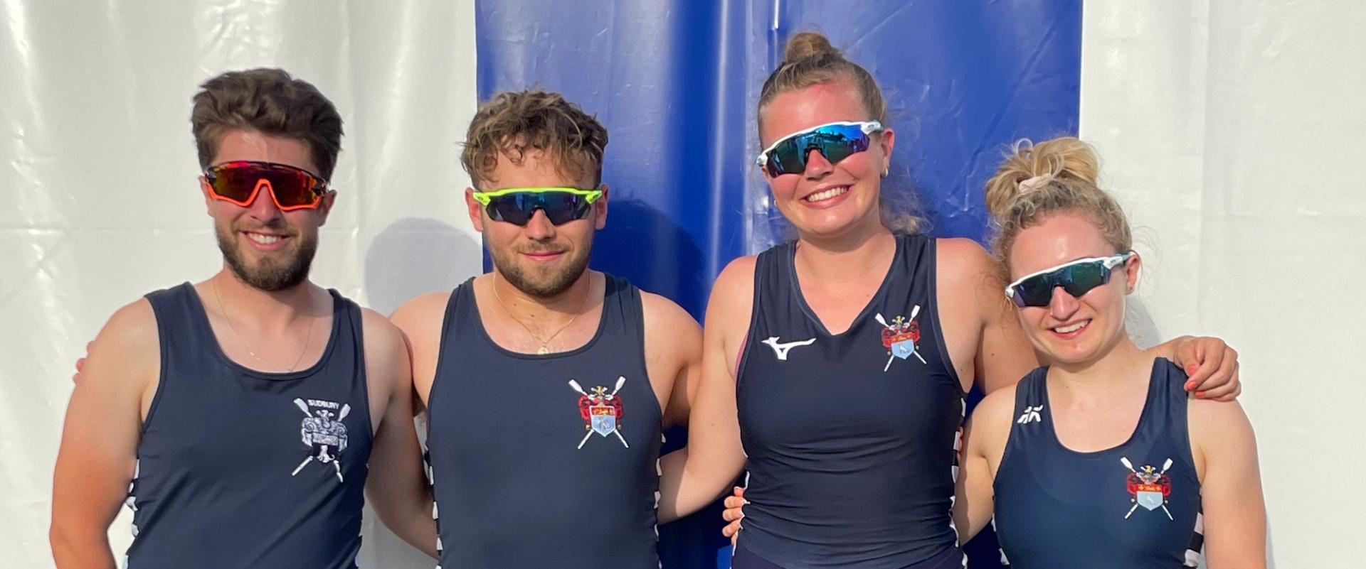 Byron Bullen, Harry Moule, Martha Bullen and Amelia Moule pose for a photo, arms linked, wearing sunglasses and all-in-ones in front of a tent at Henley. 