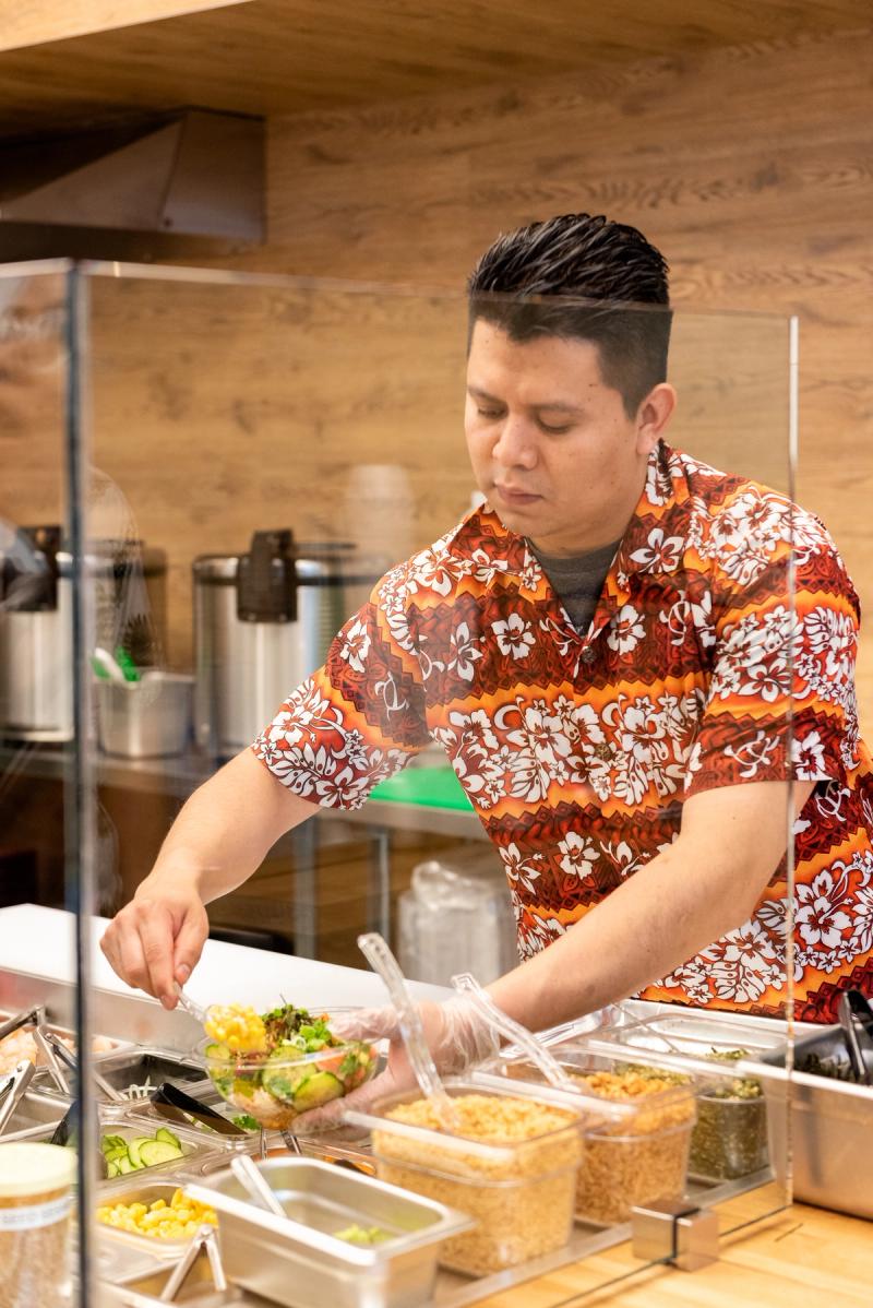 A Joy Poke employee builds a customer's poke bowl at the bar