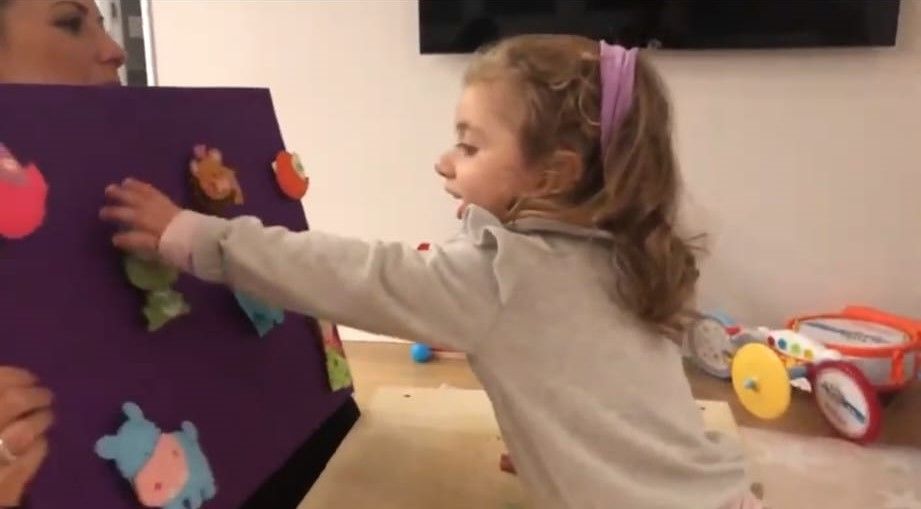 Una bambina attacca sagome di animali su un pannello di feltro