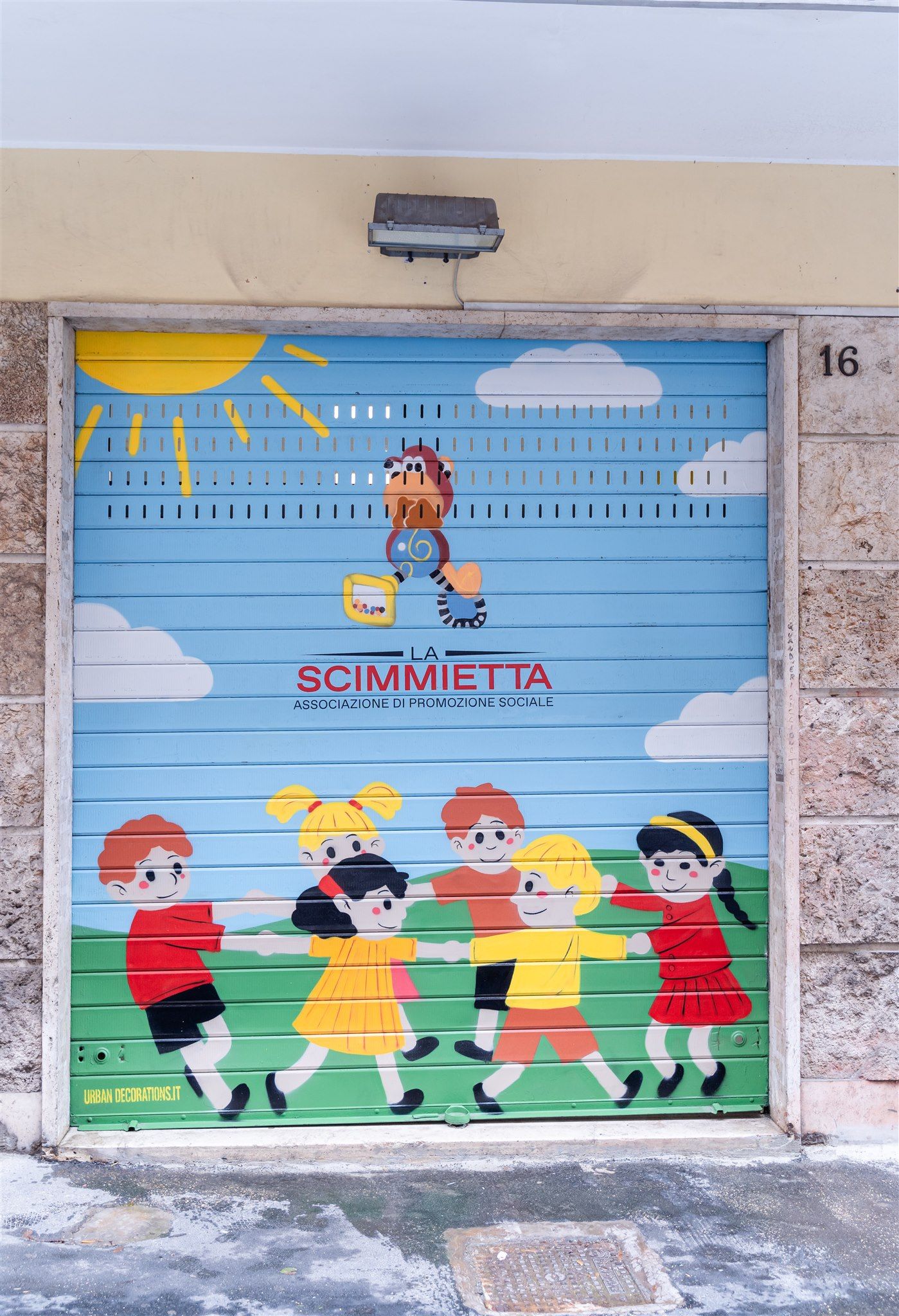 La serranda della ludoteca, dipinta con il logo della Scimmietta e i bambini in girotondo