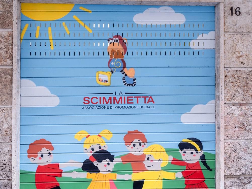 La serranda della ludoteca, dipinta con il logo della Scimmietta e i bambini in girotondo
