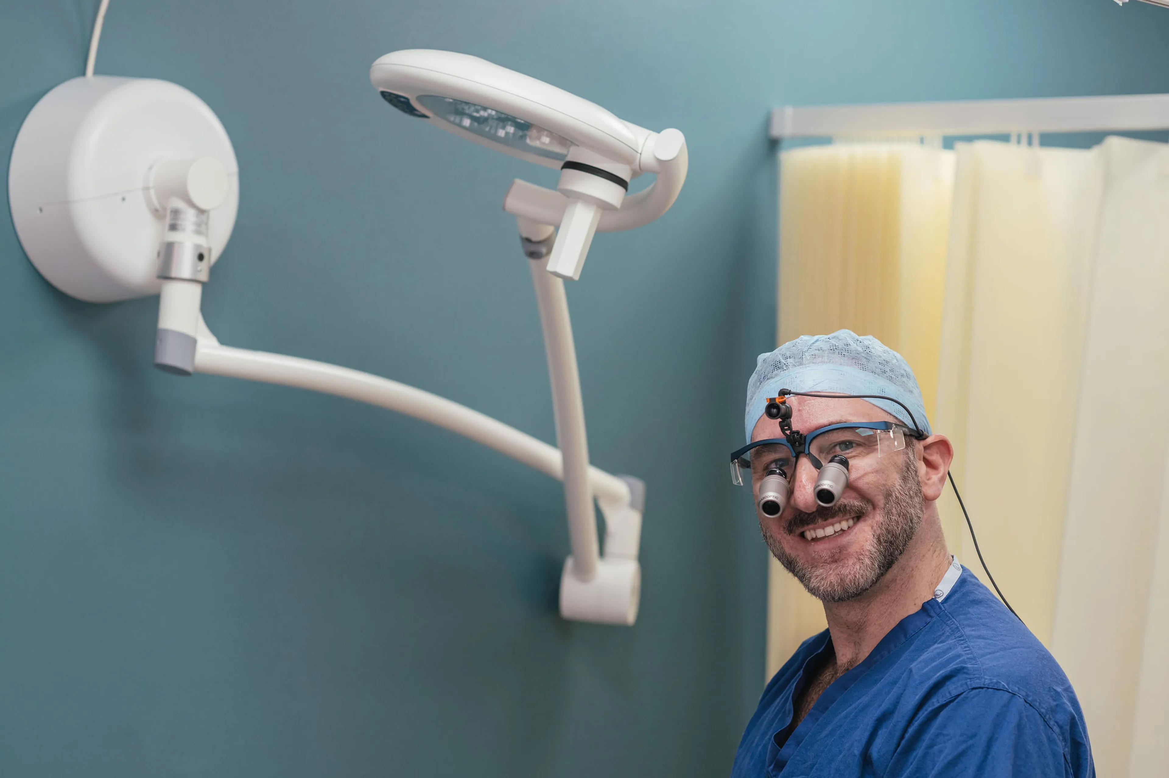 Mr Ollandini, Urological surgeon in a clinical operating theatre, wearing surgical scrubs, cap, and magnifying loupes, preparing for a delicate microsurgical procedure. The setting is clean and modern, illustrating specialist expertise in male reproductive and scrotal surgery.