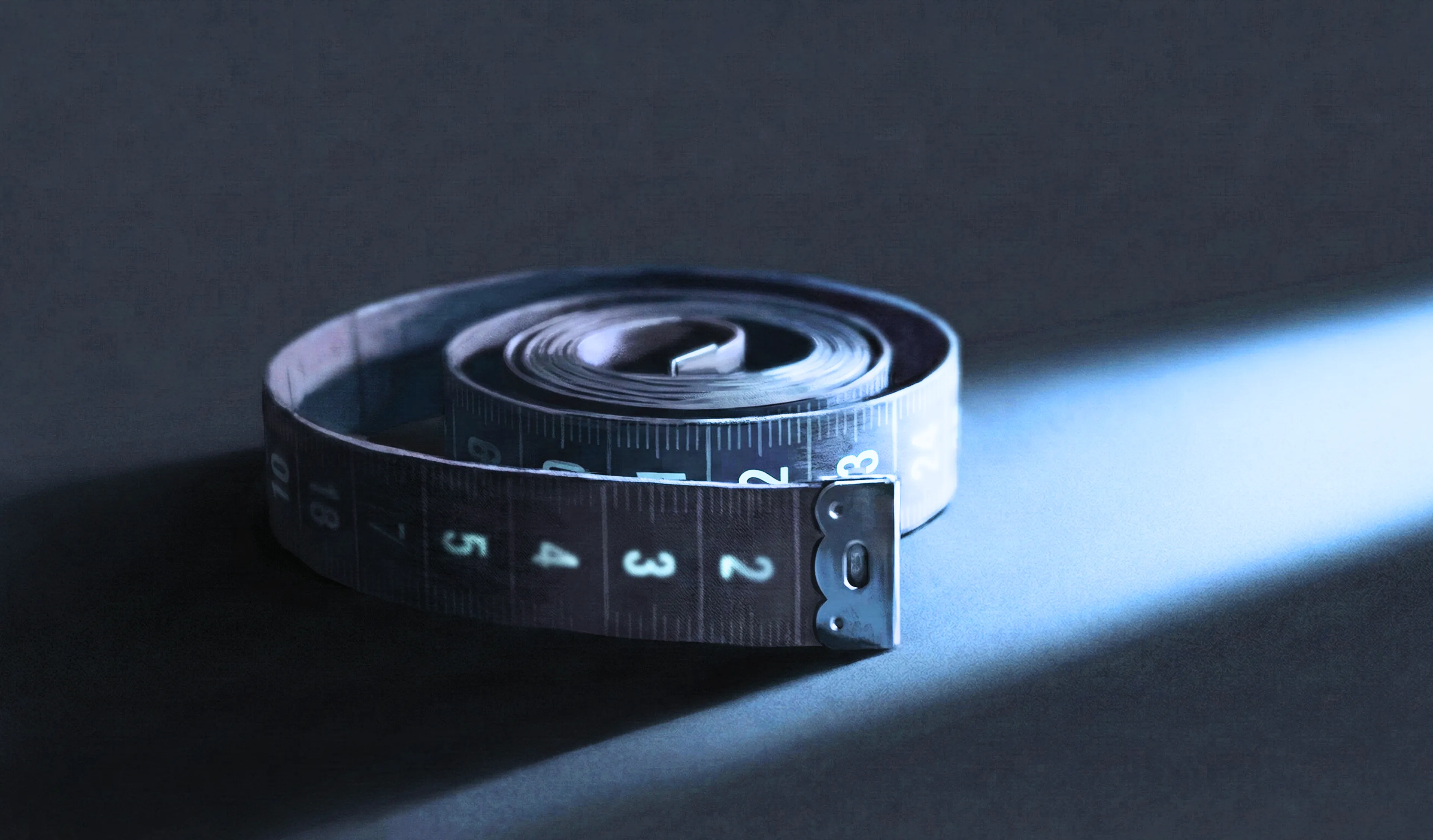 A coiled measuring tape in dramatic low lighting, symbolising the obsessive self-measurement cycle in penile dysmorphic disorder